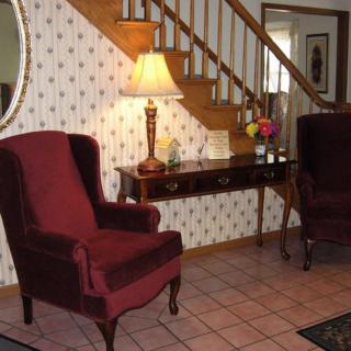 A cozy living room corner featuring two red armchairs, an elegant table with a lamp, and a staircase in the background.