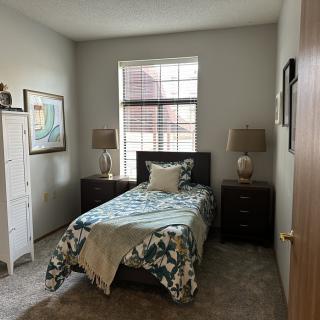 A cozy bedroom with a single bed, twin lamps, and a window letting in natural light.