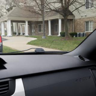 A view from the interior of a car, showcasing a building with a driveway and surrounding greenery.