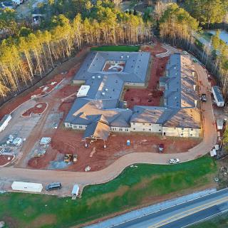Aerial view of an in-progress construction site surrounded by trees and a road.