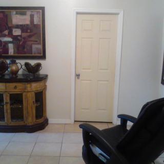 A room with a closed door, an office chair, a decorative cabinet, and artwork on the wall.
