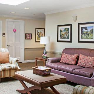 A cozy living room with a sofa, armchair, and a coffee table, decorated with wall art and a lamp.