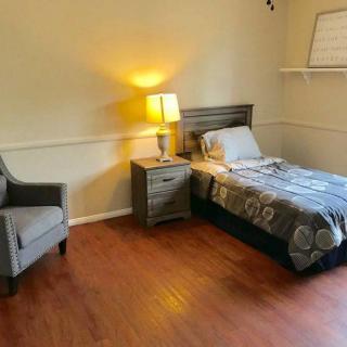 A minimalist bedroom with a single bed, wooden floor, and a cozy lamp.