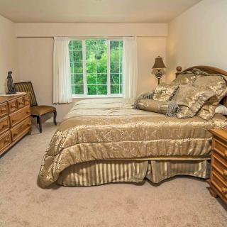 A neatly arranged bedroom with a large bed, wooden furniture, and a window with drapes.