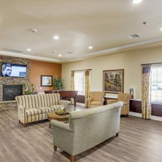 A cozy and well-furnished living room with comfortable seating, a TV above the fireplace, and large windows providing ample natural light.