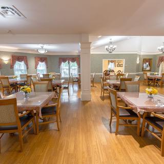 A well-lit dining room with multiple tables and chairs, featuring wood flooring and decorative elements.