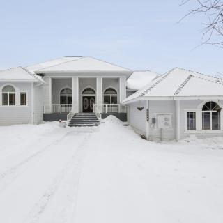 A large house with a snow-covered driveway, framed by a winter landscape.