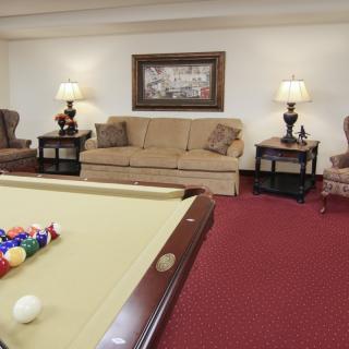 A cozy living room featuring a pool table, comfortable seating, and warm lighting.