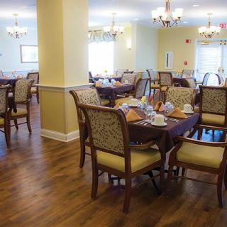 An elegant dining room with neatly arranged tables and chairs, featuring chandeliers and a wooden floor.