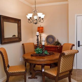 A cozy dining room with a round wooden table, upholstered chairs, and a decorative chandelier.