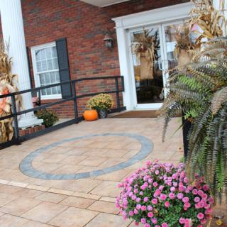 A decorated porch with autumn-themed elements, including pumpkins and flowers, at the entrance of a brick building.