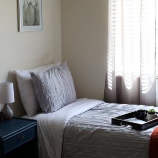 A cozy bedroom with a neatly made bed, bedside lamp, and window with blinds.