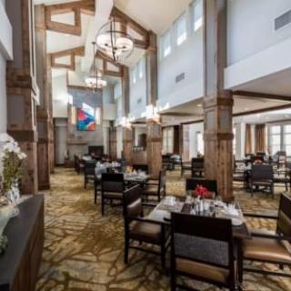 A spacious dining hall with elegant decor, featuring wooden beams, chandeliers, and neatly arranged tables and chairs.