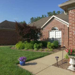 A well-maintained brick house with a landscaped garden and sidewalk under a clear blue sky.
