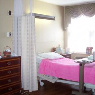 A hospital patient room with a bed covered in pink bedding and a curtain for privacy.