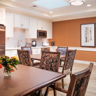 A modern kitchen and dining area featuring a wooden table with chairs, cabinetry, a microwave, and a decorative flower arrangement on the table.