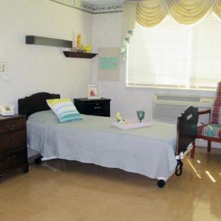 A minimalist hospital room featuring a single bed, a chair, and soft natural lighting from the window.