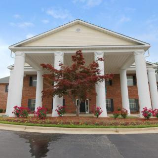 A symmetrical brick building with large white columns at the entrance and landscaped surroundings.
