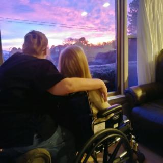 Two people share a tender moment, watching the sunset through a window.