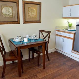 A compact kitchen and dining area featuring a wooden table set for two amidst a modern interior.