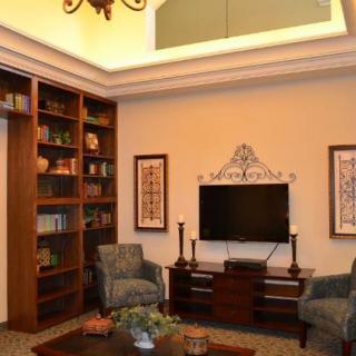 A cozy living room with a large bookshelf, comfortable armchairs, and a television mounted on the wall.