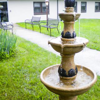 A serene outdoor scene featuring a decorative fountain surrounded by lush green grass and benches.