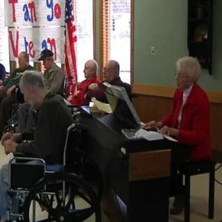 A group of seniors gathered in a nursing home for a piano performance.