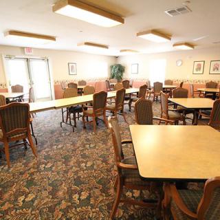 An empty dining area with arranged tables and chairs, carpeted floor, and overhead lighting.