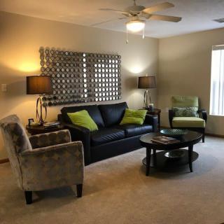 A cozy living room featuring a black sofa with green cushions, an armchair, and a coffee table, all complemented by stylish lamps and decorative wall art.