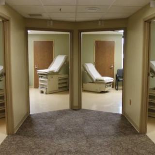 A view of a medical clinic's examination rooms with open doors, each containing an examination table.