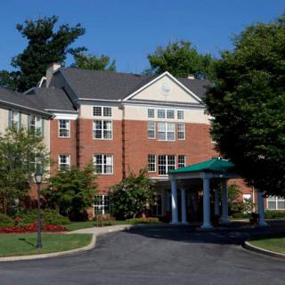 A view of a residential building with a brick exterior and an entrance driveway surrounded by trees.