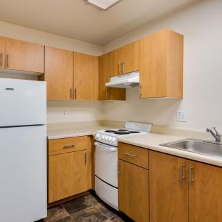 A compact kitchen with wooden cabinets, featuring a refrigerator, stove, and sink.