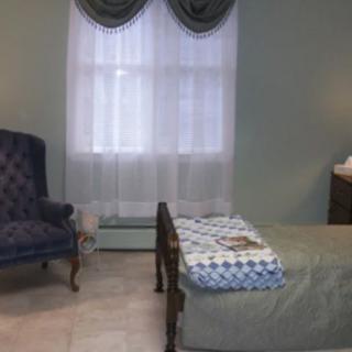 A cozy bedroom with a chair, bed, and large window covered with curtains.