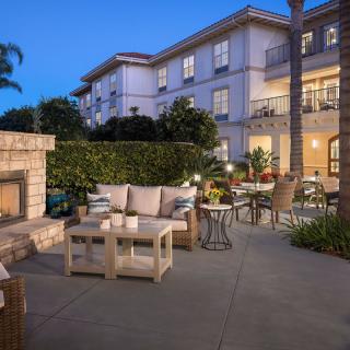 A cozy outdoor patio area with comfortable seating and a fireplace in front of an apartment building during the evening.