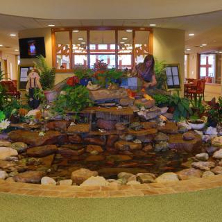 An indoor lobby featuring a decorative waterfall and pond surrounded by plants and rocks.