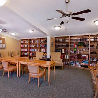 A quiet library space with tables, chairs, and bookshelves, featuring a ceiling fan overhead.
