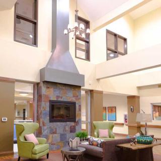 A modern lobby featuring a central fireplace, comfortable seating, and high ceilings with ample natural light.