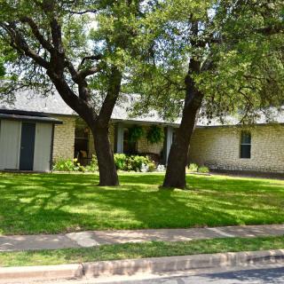 A suburban house surrounded by lush green lawn and trees.