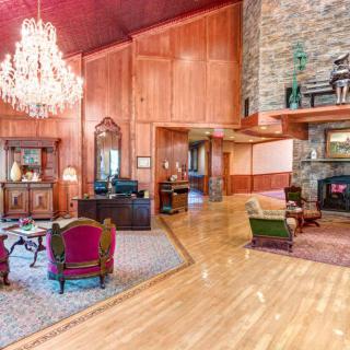 A luxurious living room featuring a grand chandelier, wood paneling, and a stone fireplace with elegant furniture.