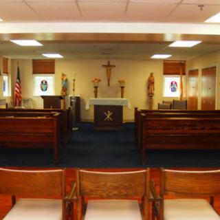 Interior view of a small chapel featuring an altar, crucifix, and pews.