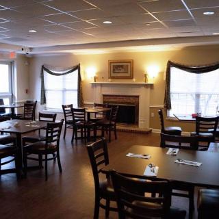 A cozy dining room with neatly arranged tables and chairs, featuring a fireplace and large windows.