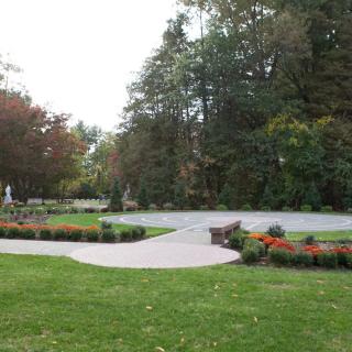 A serene park setting with a pathway surrounded by lush greenery and colorful flowers.