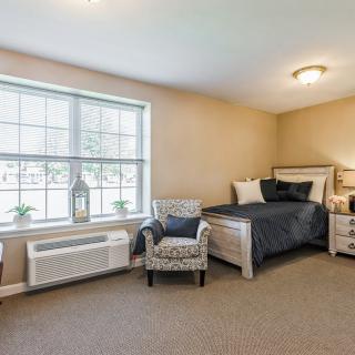 A cozy bedroom with neutral colors featuring a bed, armchair, and large window.