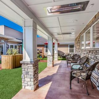 A sunny patio with outdoor seating under a covered porch, featuring stone columns and a well-maintained yard.