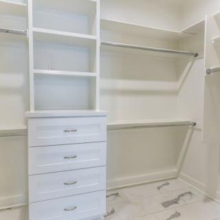An empty white closet featuring shelves, drawers, and hanging rods for organization.