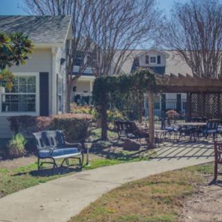 A sunny outdoor patio area with a pergola, surrounded by garden furniture and a well-kept yard.