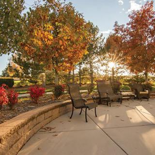 A sunny patio with chairs surrounded by colorful autumn foliage.