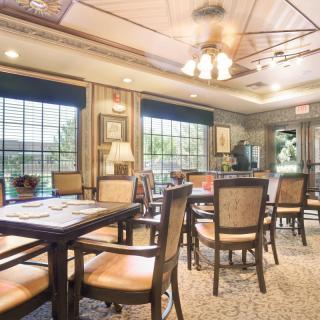 A cozy dining area filled with tables and chairs, illuminated by natural light from large windows.