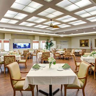 A spacious dining room with neatly arranged tables and chairs, featuring elegant decor and bright overhead lighting.