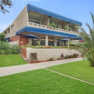 A modern building with blue awnings surrounded by lush greenery and a well-maintained lawn.